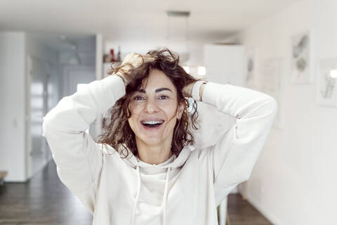 Porträt einer lachenden Frau mit Händen in den Haaren zu Hause, lizenzfreies Stockfoto