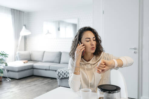 Portrait of woman looking at her smartwatch at home - KMKF01195