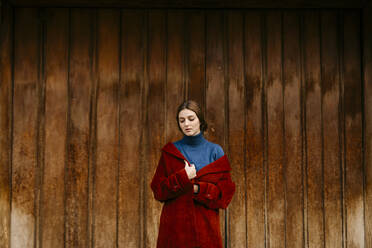 Close up portrait of woman with blue turtleneck pullover and red coat in front of a wooden door - TCEF00006