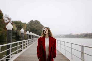Portrait of young woman wearing red coat on a bridge during rainy day - TCEF00025