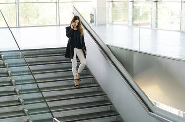 Businesswoman walking down stairs talking on the phone - DGOF00026