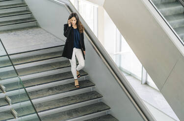Businesswoman walking down stairs talking on the phone - DGOF00027