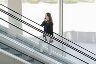 Lächelnde Geschäftsfrau auf Rolltreppe beim Telefonieren - DGOF00029