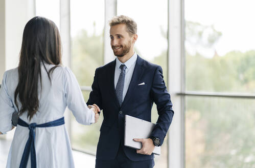 Businessman and businesswoman shaking hands at the window - DGOF00036