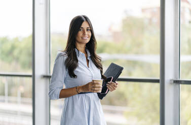 Porträt einer lächelnden Geschäftsfrau mit Tablet und Kaffee zum Mitnehmen am Fenster - DGOF00044