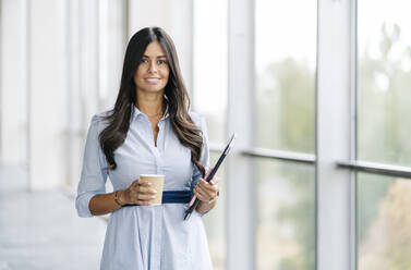 Porträt einer lächelnden Geschäftsfrau mit Tablet und Kaffee zum Mitnehmen am Fenster - DGOF00045