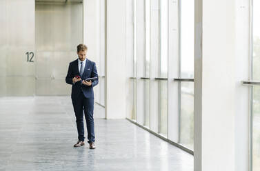 Businesman using tablet and smartphone at the window - DGOF00054