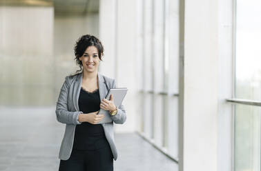 Portrait of smiling businesswoman holding tablet at the window - DGOF00063