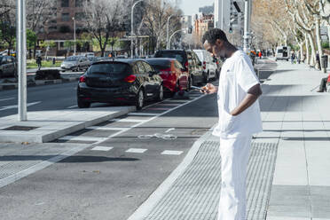 Doctor standing at roadside looking at cell phone - JCMF00342