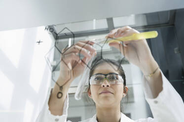 Medical student pouring liquid into test tube in front of glass wall in classroom - CUF54443