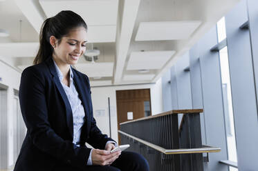 Young businesswoman using smartphone at corridor of office building - CUF54455