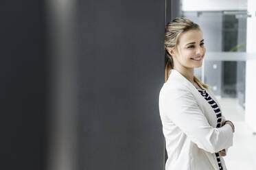 Female student leaning against grey wall in office building - CUF54468