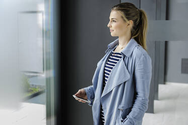 Female student with smartphone at corridor of office building - CUF54473