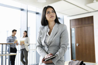 Young businesswoman in office, colleagues talking in background - CUF54505