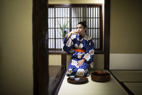 Japan, Young woman wearing traditional kimono drinking tea in ryokan - ABZF02898