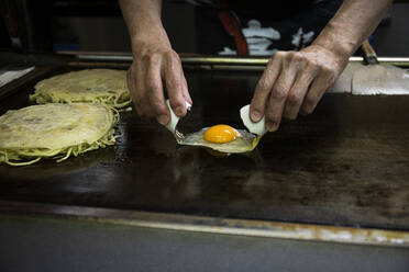 Japan, Kyoto, Nahaufnahme eines Kochs bei der Zubereitung von Okonomiyaki im Restaurant - ABZF02950