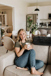 Woman relaxing on sofa with warm beverage - ISF23660