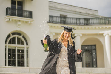 Absolventin mit geöffneter Flasche Champagner auf dem Campus - ISF23732