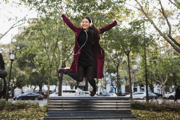 Portrait playful exuberant woman jumping off urban city bench - FSIF04515