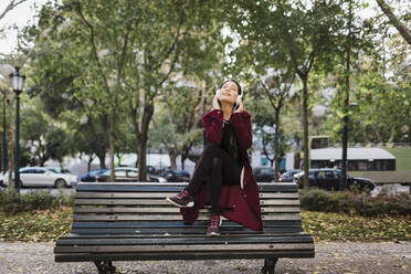 Carefree woman listening to music with headphones on urban park bench - FSIF04517