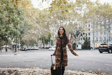 Porträt glücklicher weiblicher Tourist mit Koffer auf städtischer Herbststraße - FSIF04523
