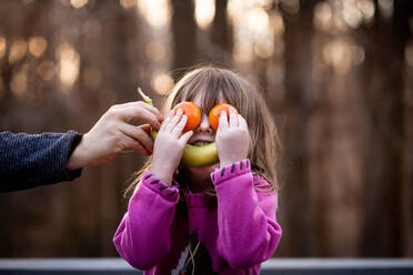 Young girl puts fruit on face to make silly face outside - CAVF72999