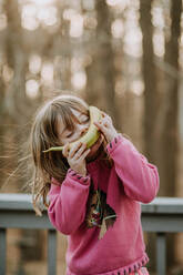 Young girl with banana on her face smiling outside - CAVF73002