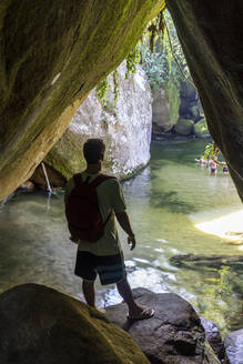 Mann in einer Höhle mit Blick auf einen schönen grünen Fluss in Serra dos Órgãos - CAVF73011