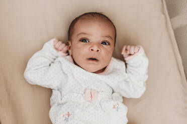 Dark-haired month old baby with wide open eyes lying in crib - CAVF73031