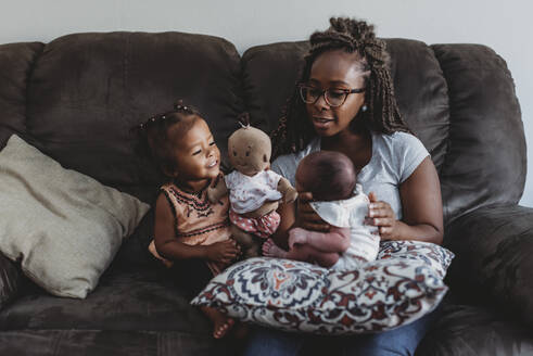 Ethnische Mutter mit Brille auf Couch mit multirassischer Tochter und Neugeborenem - CAVF73034