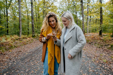 Frauen sehen sich in einem abgelegenen Wald ein Streaming-Video auf einem Smartphone an - CAVF73066