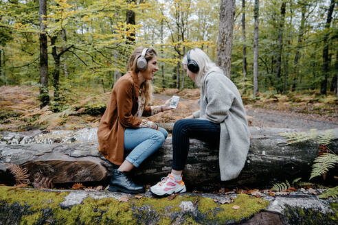 Zwei Frauen streamen ein Video auf einem Smartphone in einem abgelegenen Wald - CAVF73075