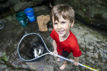 Young boy holding fishing net with fish - CAVF73106