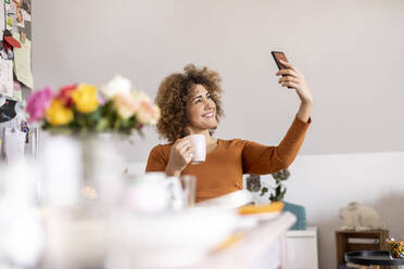 Frau hält Kaffeetasse und nimmt ein Selfie zu Hause - FMKF06072