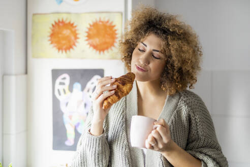 Frau isst Croissant und trinkt Kaffee zu Hause - FMKF06076