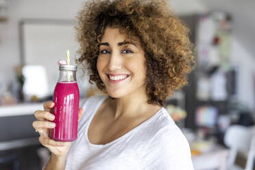 Portrait of smiling woman with a smoothie at home - FMKF06077