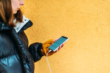 Junge Frau benutzt ihr Smartphone, während sie an einer gelben Wand steht - CAVF73243