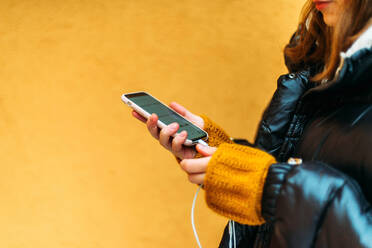 Young woman using smart phone while standing against yellow wall - CAVF73245