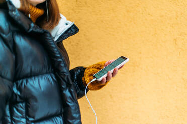Junge Frau benutzt ihr Smartphone, während sie an einer gelben Wand steht - CAVF73246