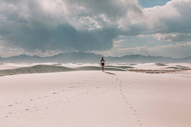 Woman walking in the desert as the sun shines through a cloud - CAVF73278