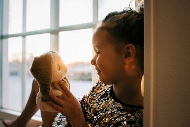 Junges Mädchen schaut liebevoll auf ihr Spielzeug zu Hause bei Sonnenuntergang - CAVF73343