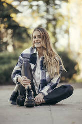 Porträt einer lächelnden jungen Frau, die im Freien auf dem Boden sitzt - MTBF00299