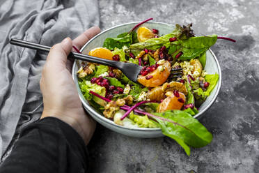 Eine Hand hält eine Schüssel mit Wintersalat, Mandarinen, Walnüssen, Feta und Granatapfelkernen - SARF04428