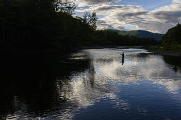 Ein einsamer Mann, der bei Sonnenuntergang in einem Fluss angelt. - CAVF73416