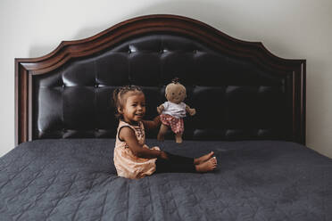 2 Jahre altes gemischtrassiges Mädchen spielt mit Puppe auf dem Bett der Eltern - CAVF73426