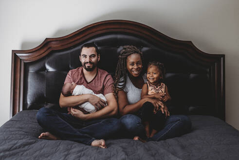 Gemischtrassige Familie zusammen im Bett - Vater, Mutter, Kleinkind und 2 Jahre alt - CAVF73441