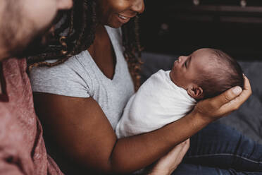 Parents smiling at multiracial infant swaddled in white blanket - CAVF73453