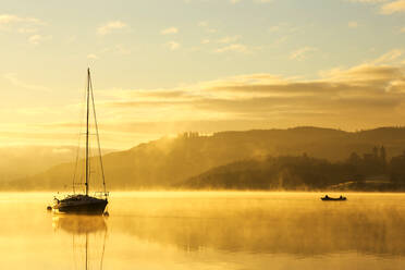 Sonnenaufgang über Männern, die in einem Boot auf dem Lake Windermere in Ambleside, Lake District, Großbritannien, fischen. - CAVF73486