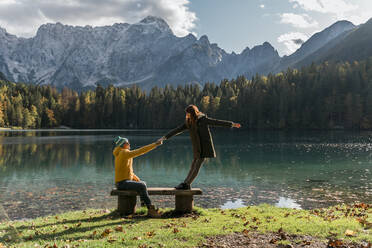 Händchenhaltendes Paar auf einer Bank in Laghi di Fusine, Friaul-Julisch Venetien, Italien - MAUF03202