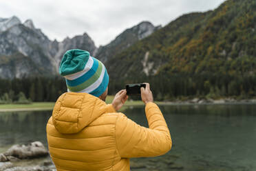 Wanderer, der sein Smartphone benutzt und ein Foto an den Laghi di Fusine macht, Friaul-Julisch Venetien, Italien - MAUF03215